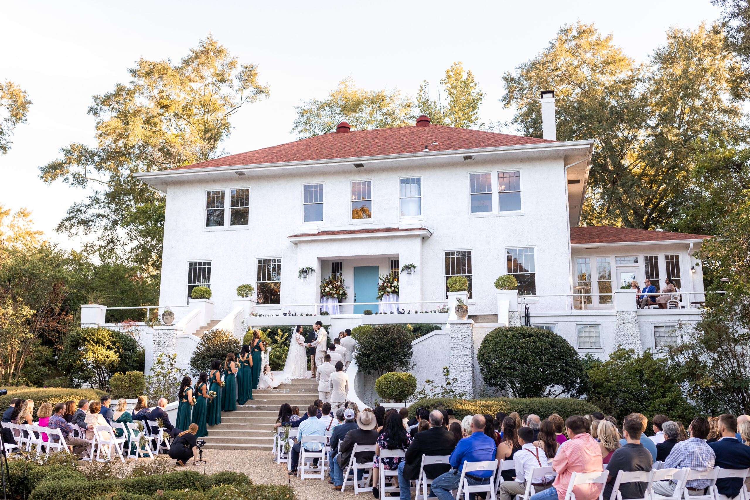 Historic estate wedding ceremony at The Crawford House in Hattiesburg, MS featuring an outdoor staircase ceremony and white garden chairs by Dear Magnolia Films.
