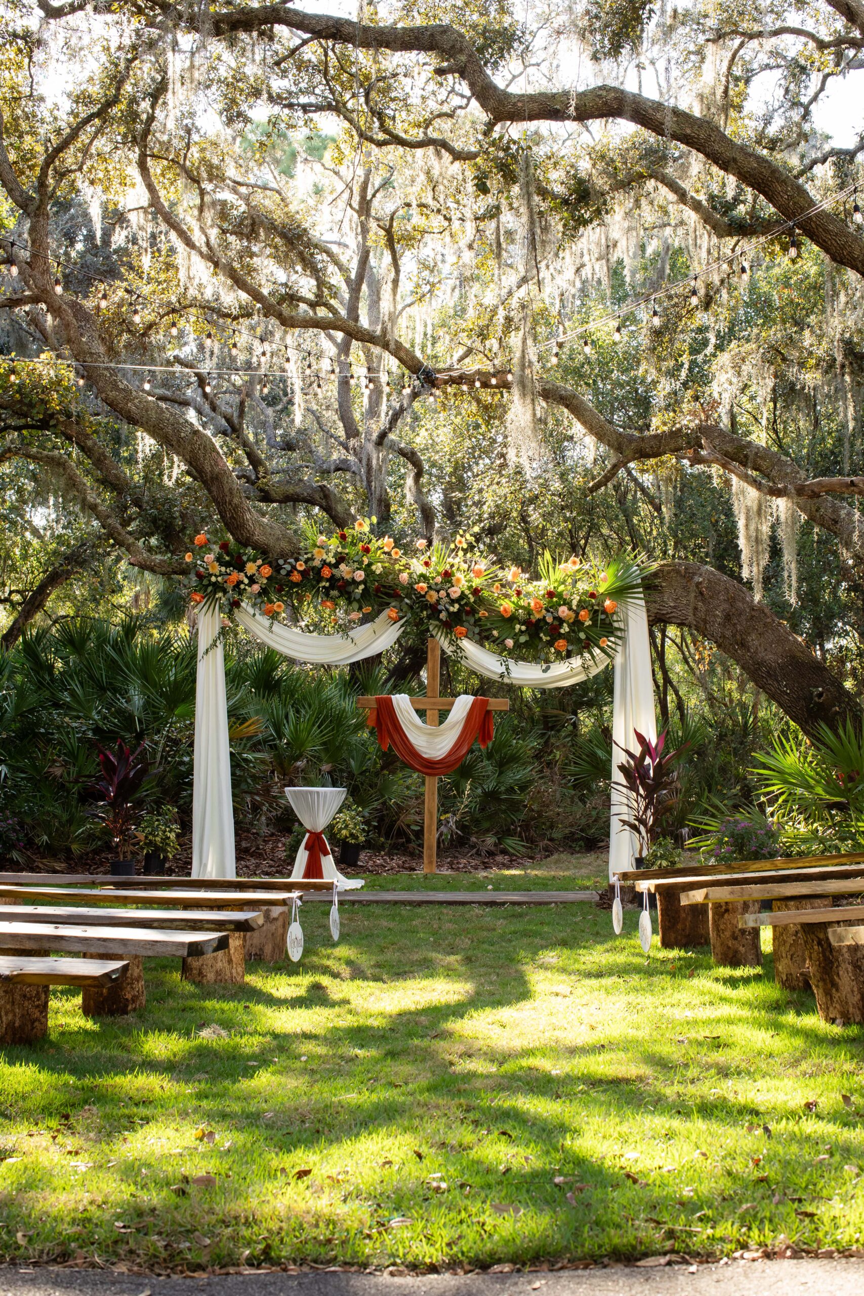 A central wooden cross draped in fabric at the Rustic Grace Barn outdoor altar, highlighting a traditional faith-based ceremony setting in Davenport, FL by Dear Magnolia Films.