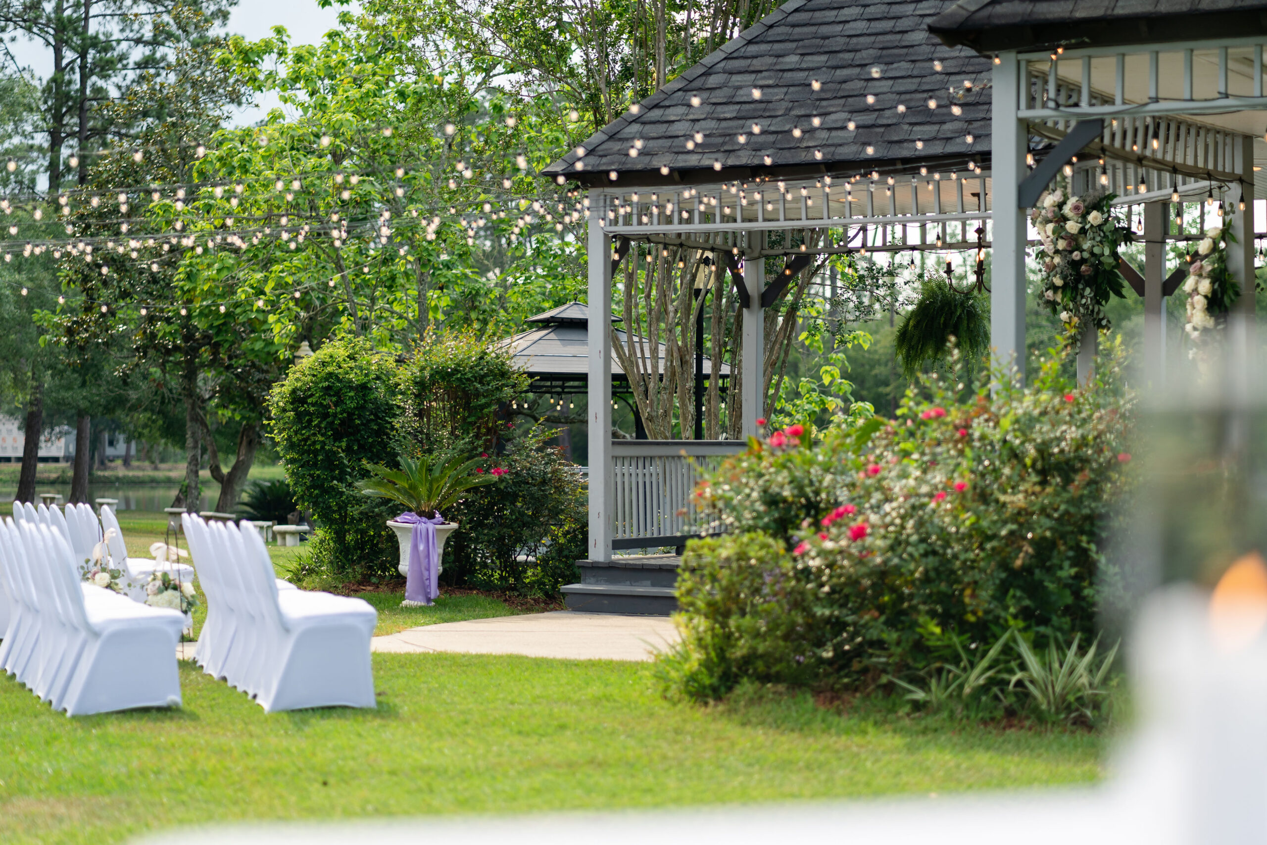 Outdoor wedding ceremony setup at Lynhaven Events in Hammond Louisiana with white chair covers and a decorated gazebo featuring string lights and floral arrangements.