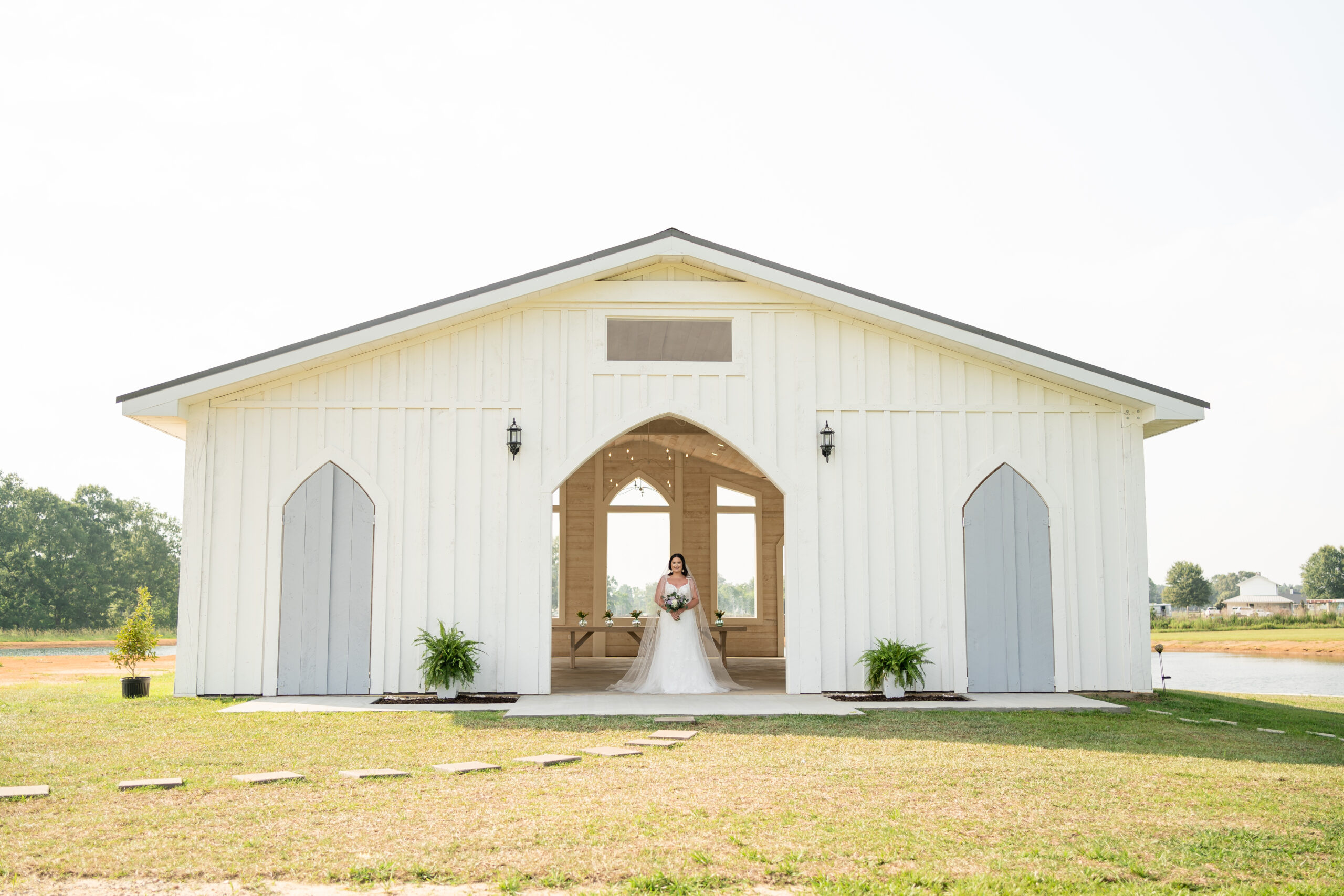 Bridal portrait under the central open archway of the white barn chapel at Wolf Hill Wedding Venue and Event Center in Mississippi by Dear Magnolia Films.