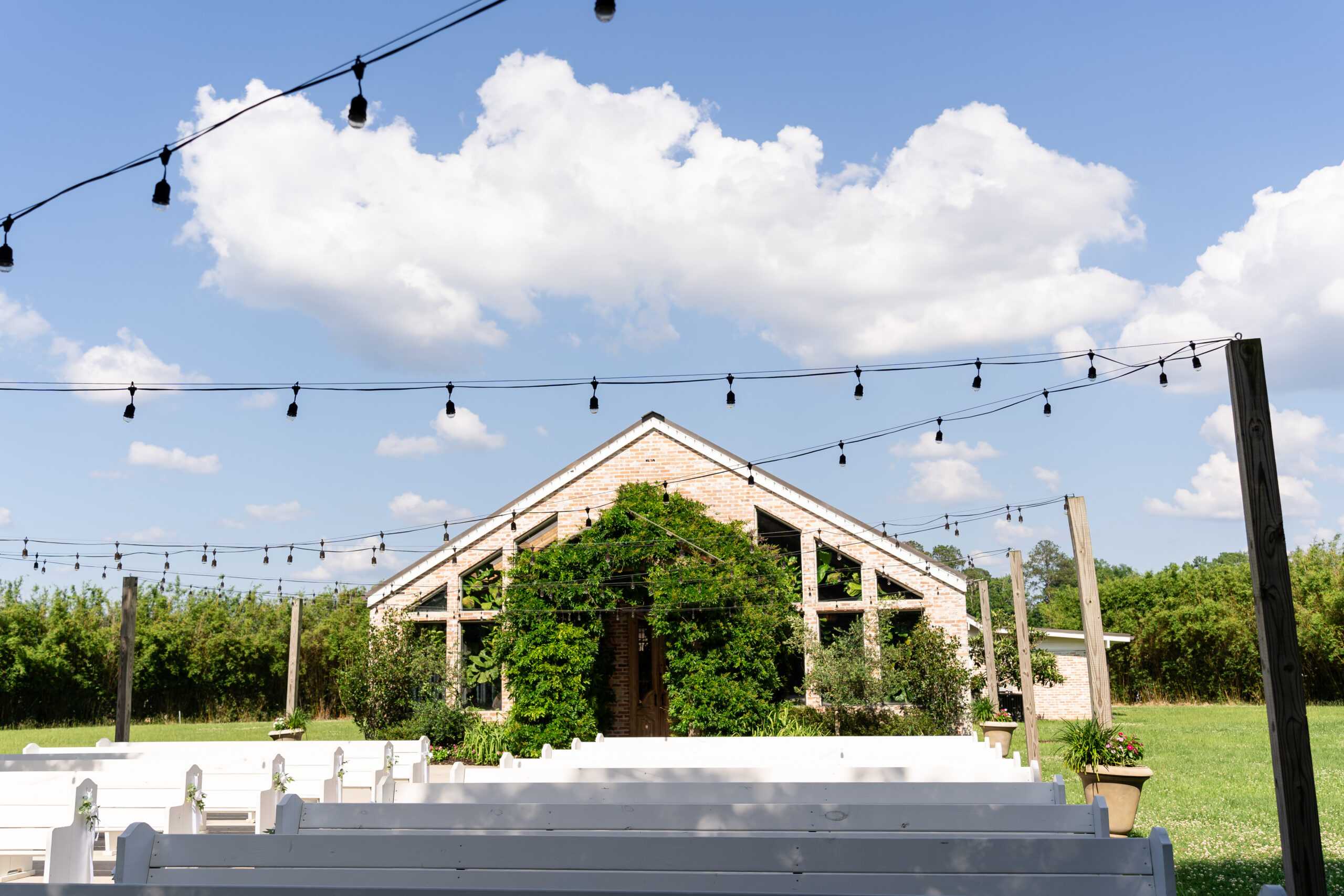 Outdoor wedding ceremony venue at The Greenery in Amite City LA featuring white pews and string lights by Dear Magnolia Films.